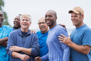 Multi-ethnic group of men standing together, smiling, supporting one another. Mixed ages ranging from 20s to 70s.